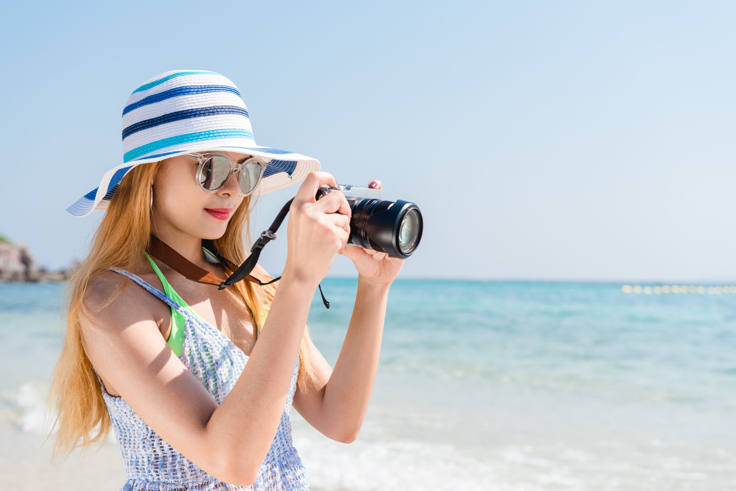 Ragazza in spiaggia con occhiali da sole pareo cappello e macchina fotografica durante le vacanze in calabria in totale relax